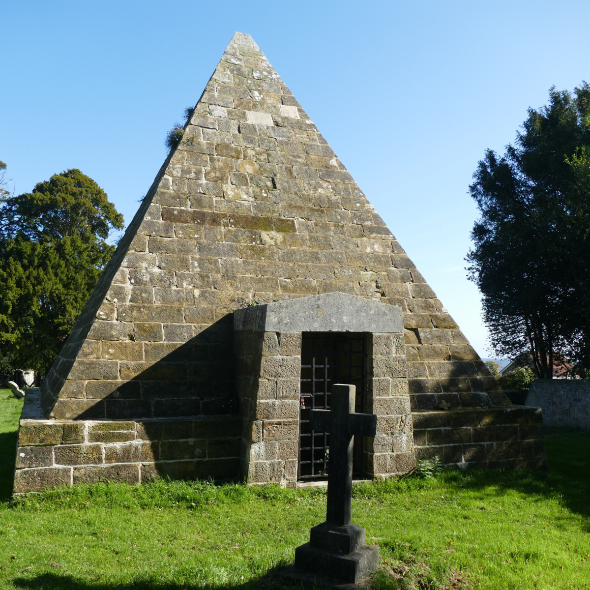 Stone pyramid folly at Brightling, part of Mad Jack’s Follies, with a small entrance set in a grassy area under a blue sky